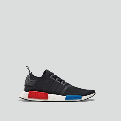 Side view of a black Adidas NMD R1 sneaker with a white sole featuring red and blue EVA plugs, displayed against a plain light gray background.