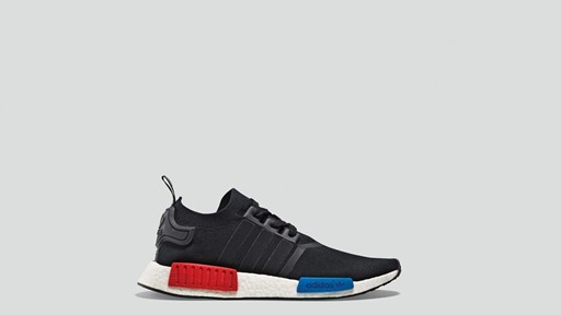 Side view of a black Adidas NMD R1 sneaker with a white sole featuring red and blue EVA plugs, displayed against a plain light gray background.