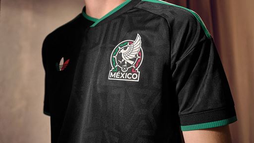 Close-up of a person wearing a black Mexico soccer jersey with green trim on the collar and sleeves, featuring a winged soccer ball logo and the word "México" on the chest.